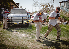 Many Team Rubicon volunteers took part in rescue efforts in the aftermath of Hurricane Harvey, which ravaged parts of southeastern Texas in August 2017. Here, former Army Green Beret Brighton Timmins (L) and firefighter Samson Rivera pull a disabled truck out of the way of a home in Rockport, Texas. (<em>Photo by</em> <em>Matt Mateiescu</em>