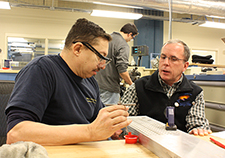 Cooper (right) explains to retired Marine Gunnery Sgt. James Joseph part of a device that is being made in HERL's Advanced Inclusive Manufacturing Training program. The device is the PathLoc Mobile caster. 