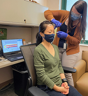Neurofeedback specialist Dr. Caitlin Tyrrell demonstrates placing electrodes on research coordinator Kim Schaper's scalp. The location of electrodes corresponds to specific brain regions associated with symptoms of mild traumatic brain injury (mTBI). 